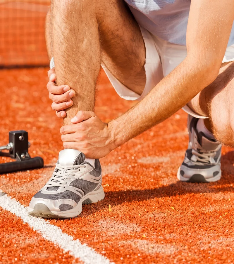 Athlete on a tennis court holding an injured ankle